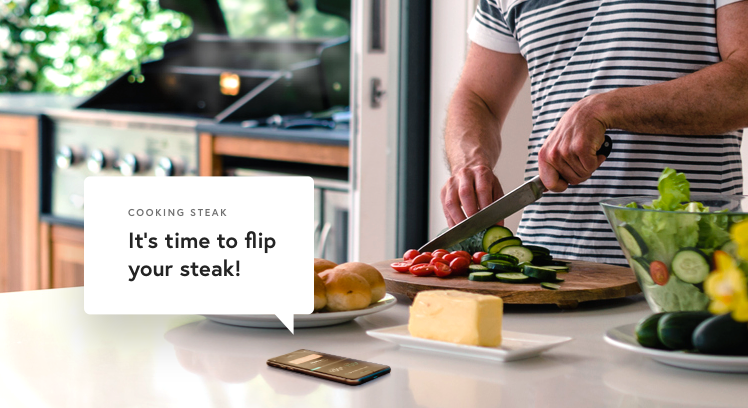 Someone chopping vegetables. A conversational bubble above a smartphone nearby reads, &quot;It&#x27;s time to flip your steak!&quot;