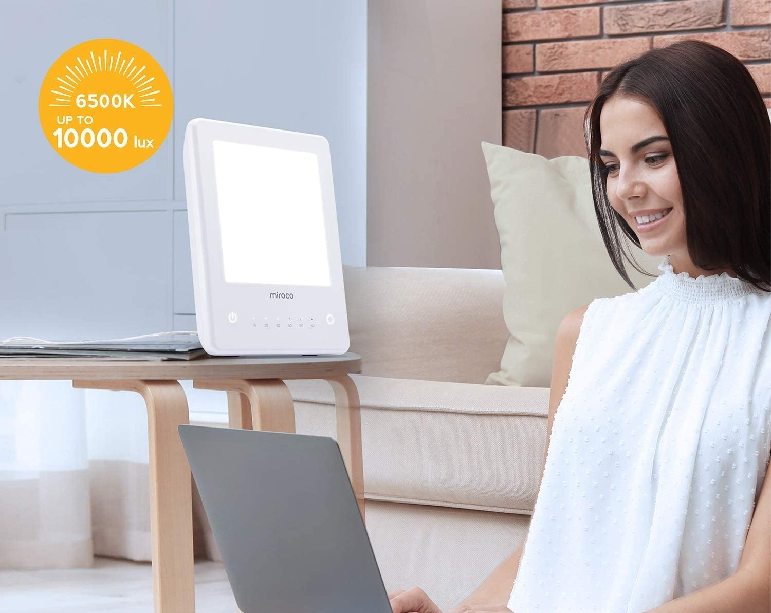 A model working on a computer next to the small rectangular light propped on a table 