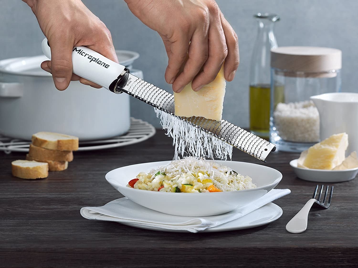 Hand using the microplane to grate a block of cheese on pasta