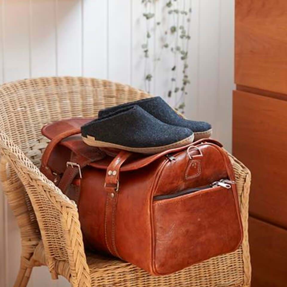 A pair of slip-on Glerups slippers set atop a leather bag