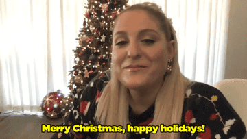 Meghan sitting in front of a lit Christmas tree saying, &quot;Merry Christmas, happy holidays!&quot;