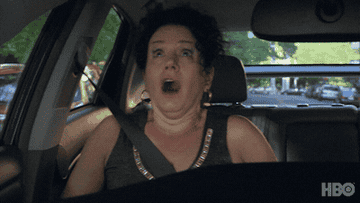 A woman screaming in a car and the man driving screaming back and covering his ears