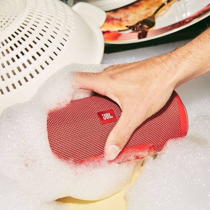 Person putting the speaker in a sink full of soapy water to show its waterproof capabilities 