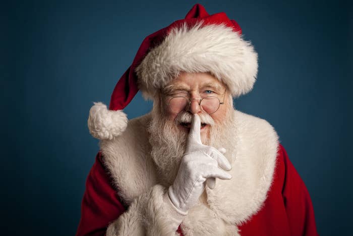 Santa winking and holding one finger over his mouth