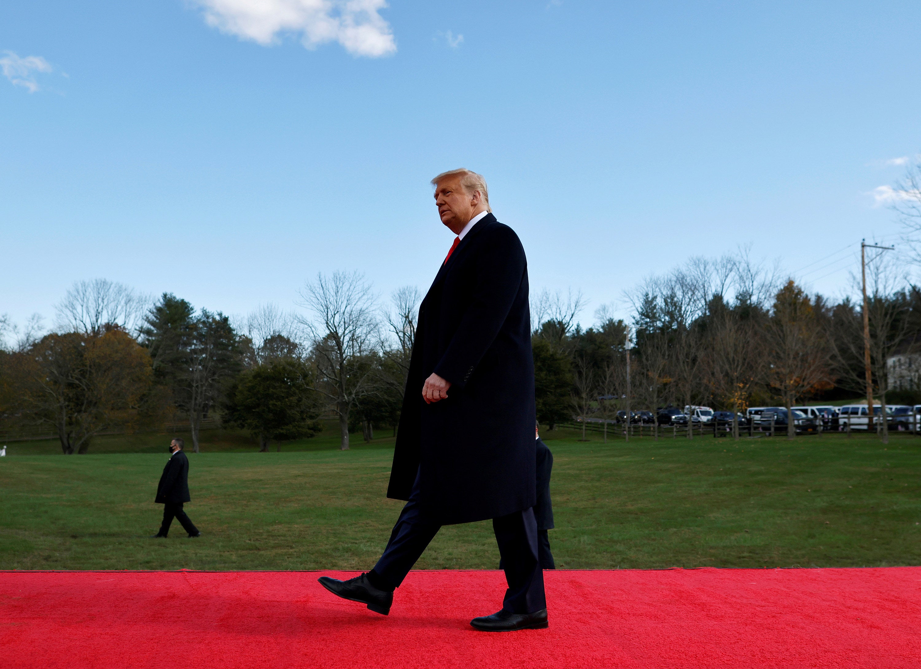 Donald Trump andando em um tapete vermelho sobre um gramado.. 