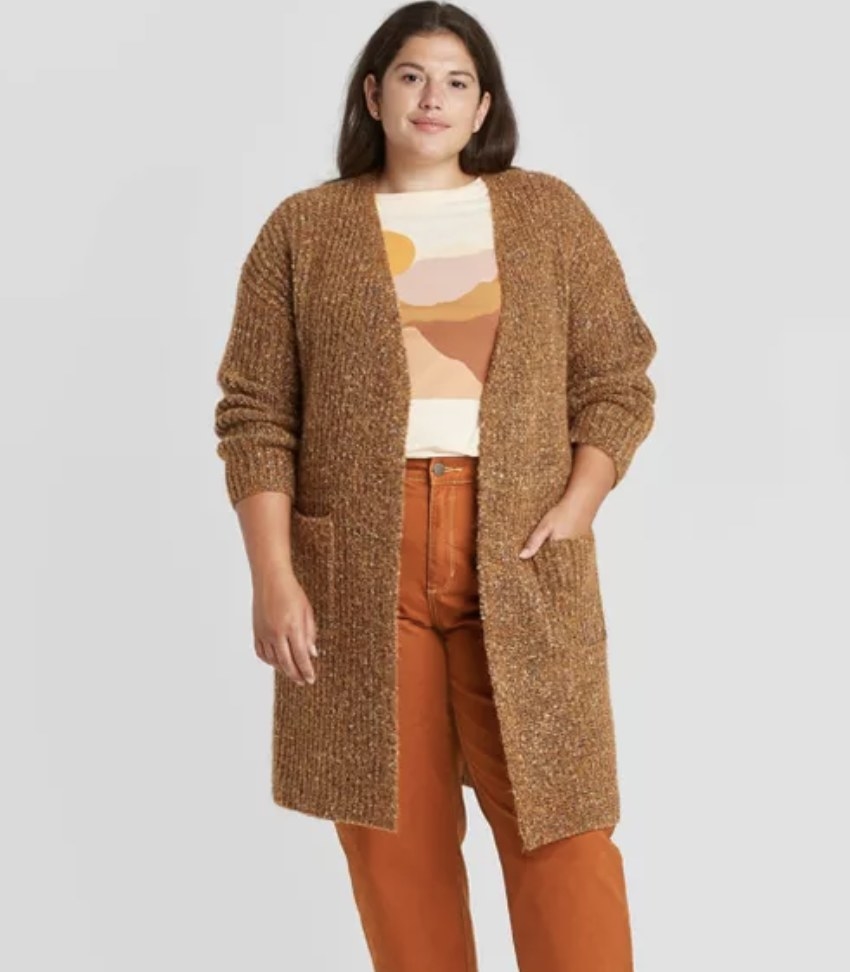 model wears longer brown cardigan and orange pants 