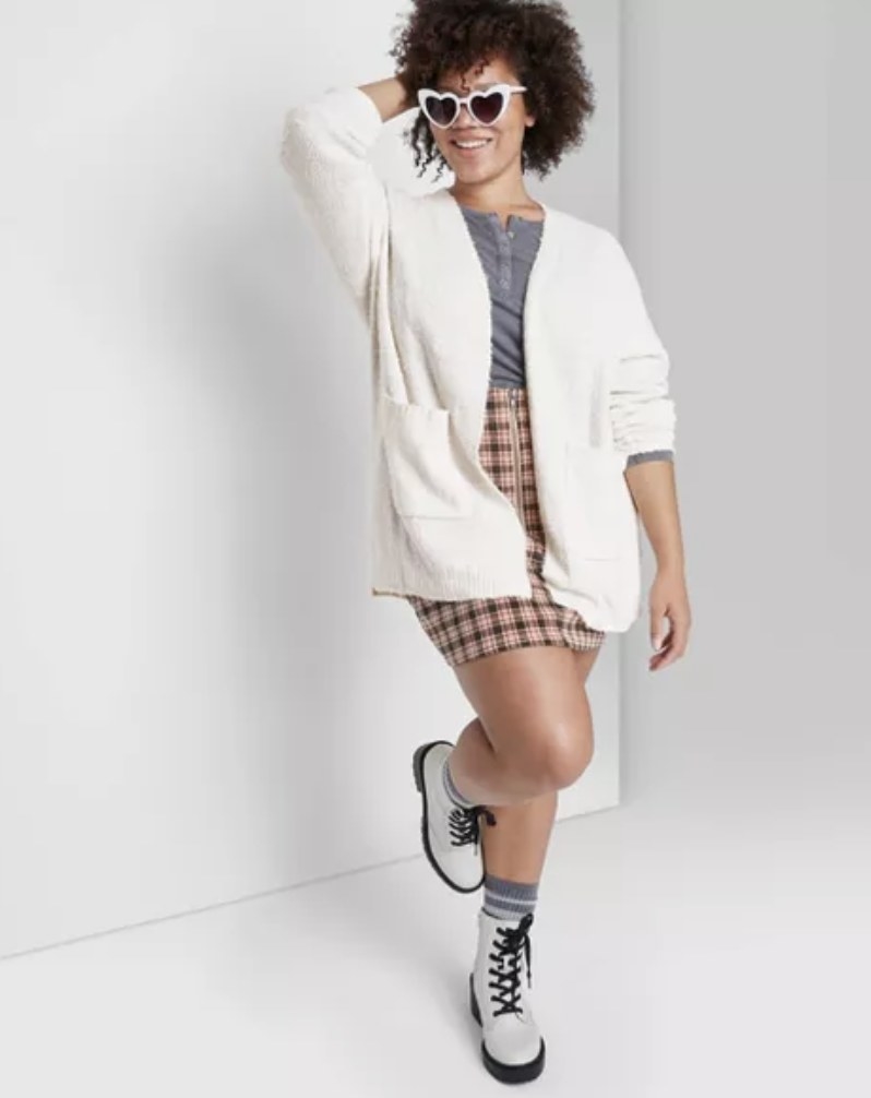 model wears white fuzzy cardigan with plaid skirt