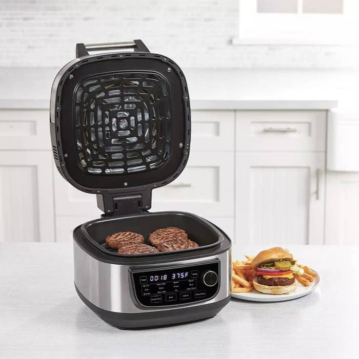 The air fryer with burger patties inside and next to a plate with a burger and fries on top
