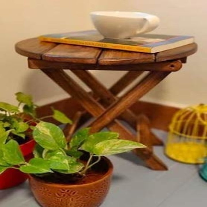 A wooden table with a round top and crossed legs.