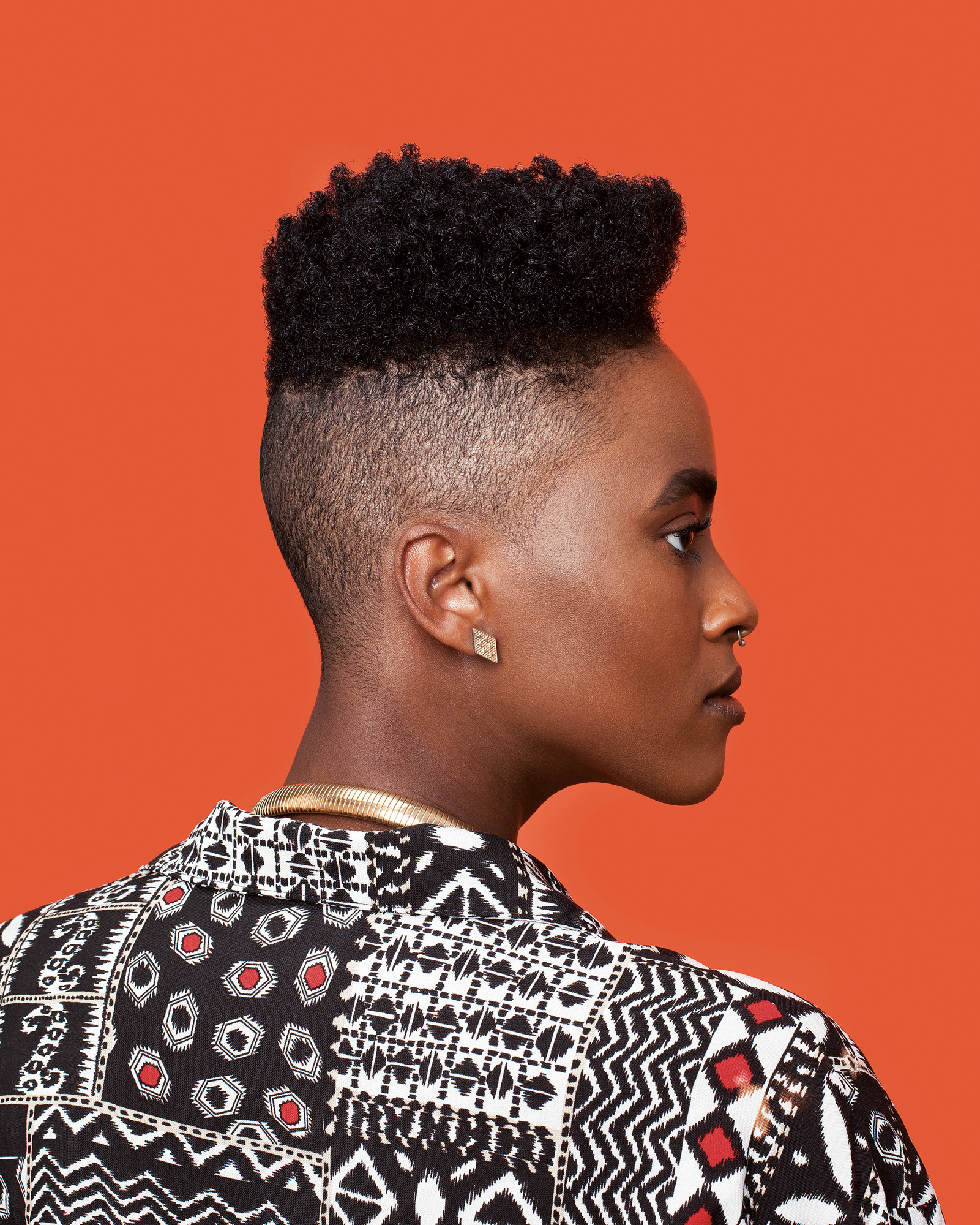 A side profile of a Black woman with great hair looks to the right against an orange background