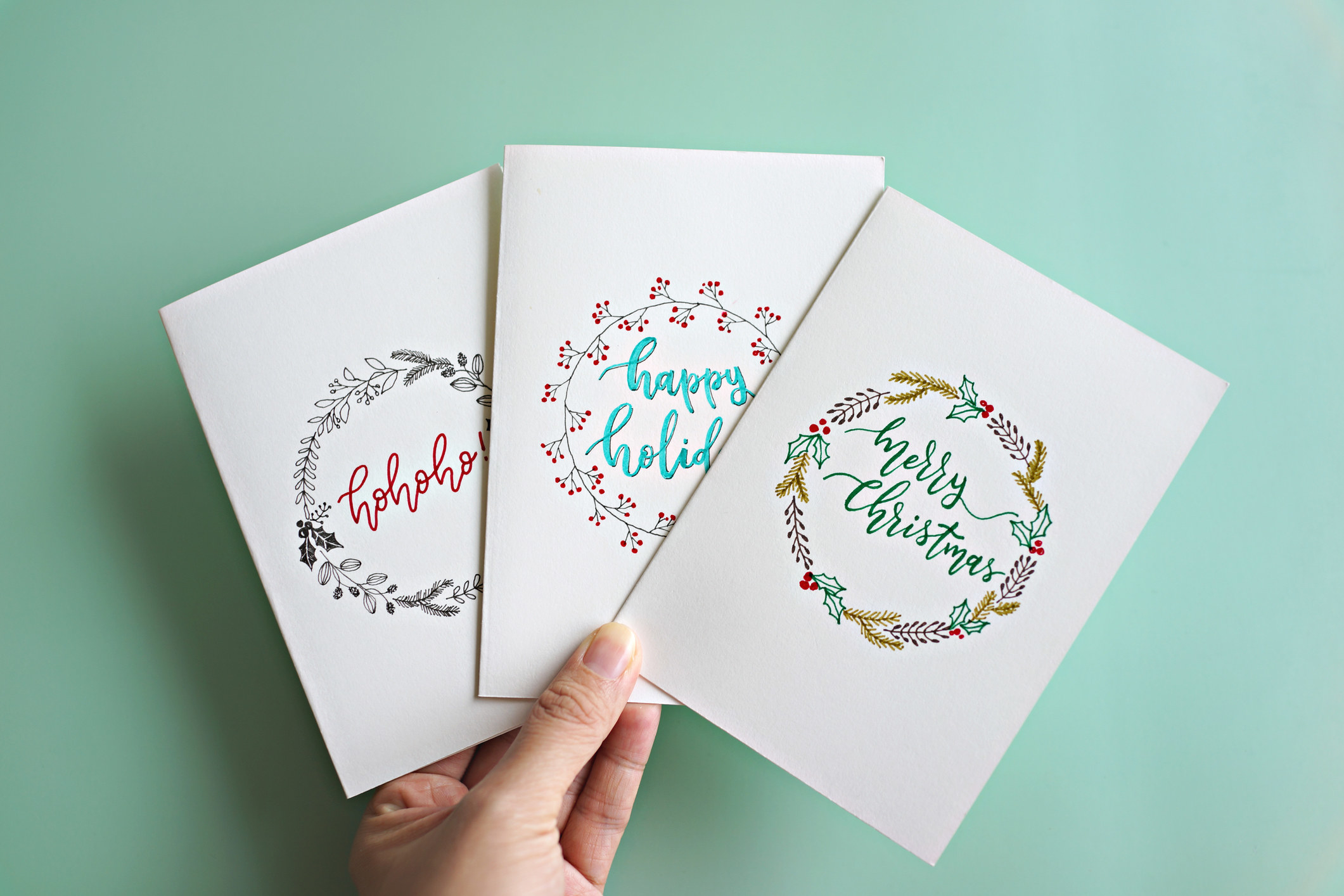 A person&#x27;s hand holding three holiday cards