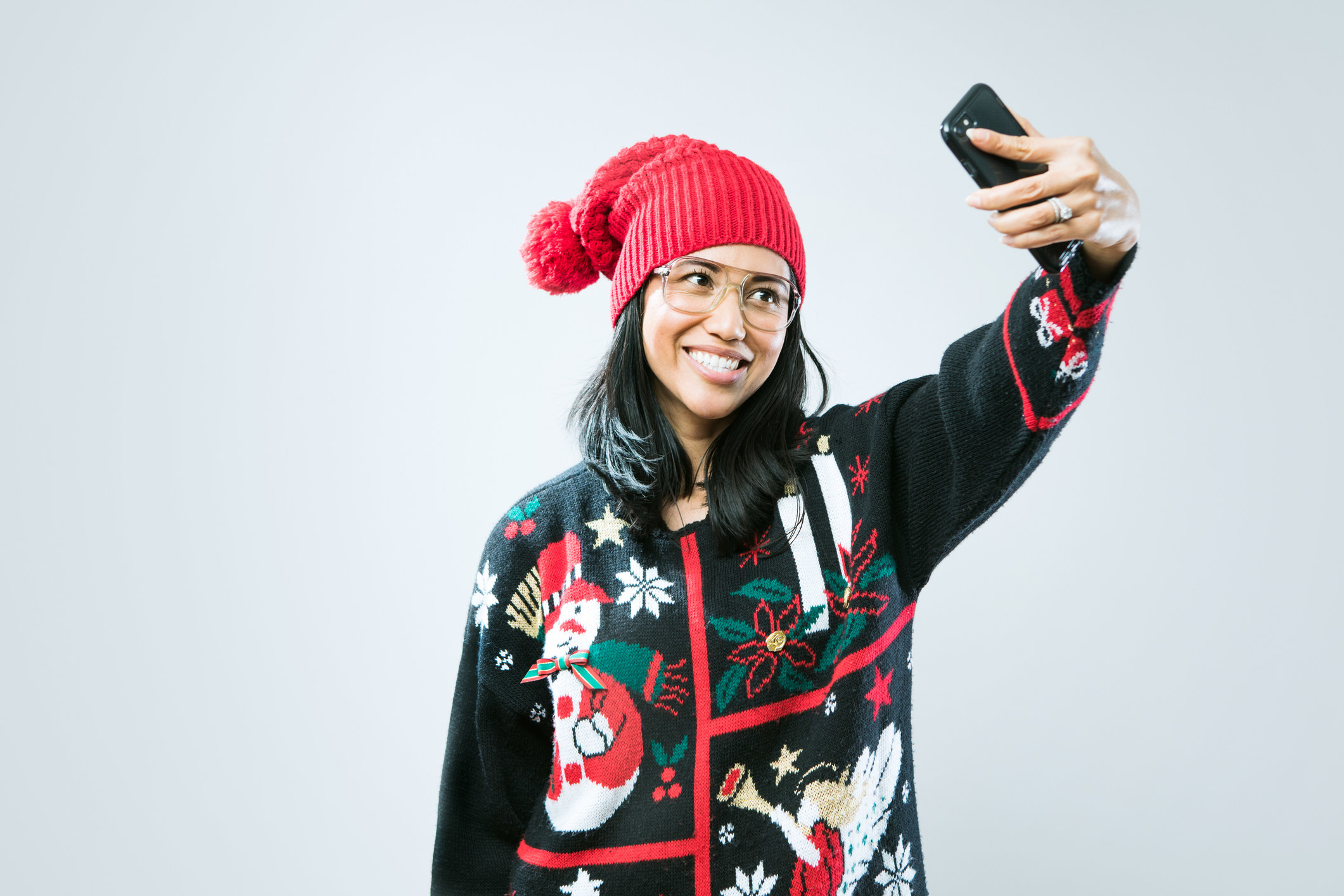 A person wearing a holiday-themed sweater and taking a selfie of their outfit