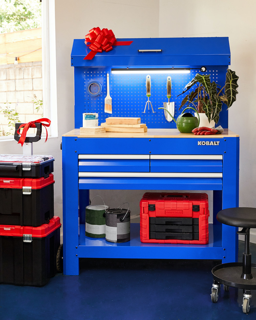 A photo of the Kobalt 45-inch x 36-inch 3-Drawer Hardwood Work Bench with gardening and home supplies.