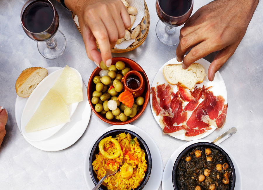 Two hands reaching for plates of Spanish tapas.
