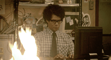GIF of actor Richard Ayoade in the show &#x27;The IT Crowd&#x27; continuing to type as a fire rages near him 