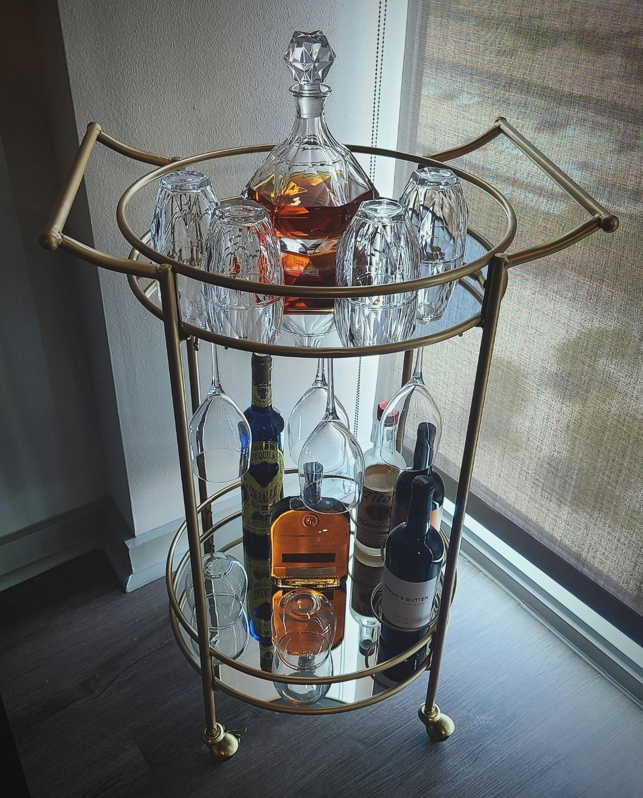 reviewer's gold bar cart with two round mirrored shelves whose top shelf has a wine glass hanger underneath