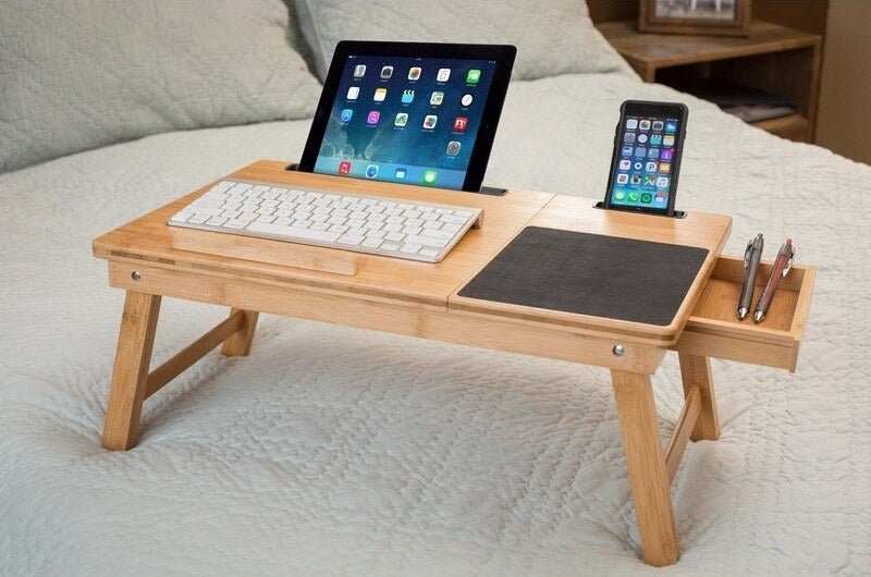 A wooden lap desk with a computer and phone on it
