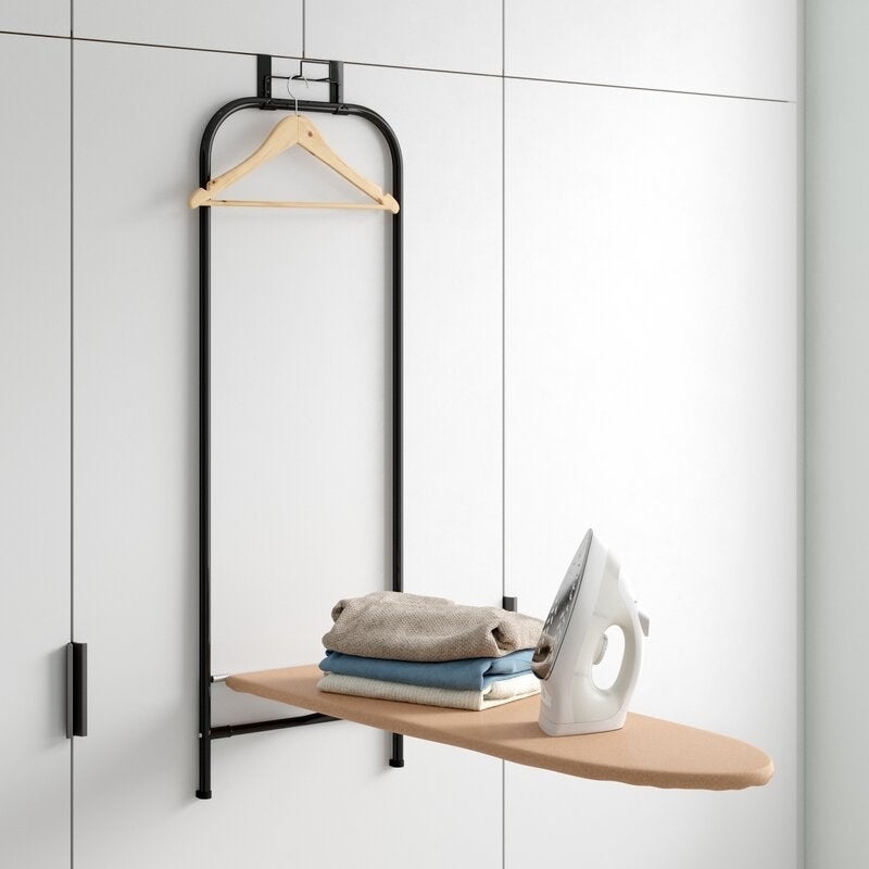 A white wall with an ironing board, iron and clothes attached to it