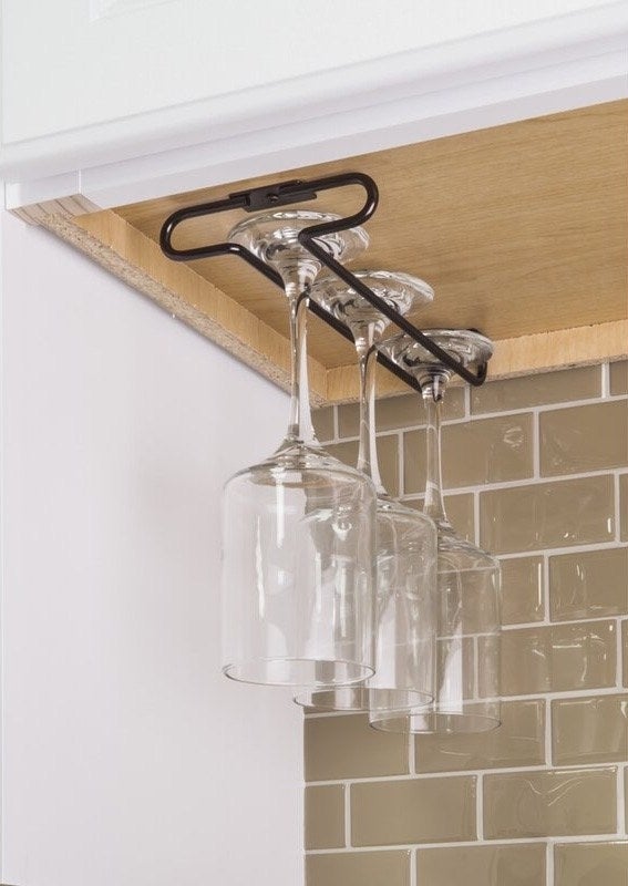 A wine glass holder with three glasses of wine hanging upside down inside a kitchen cabinet