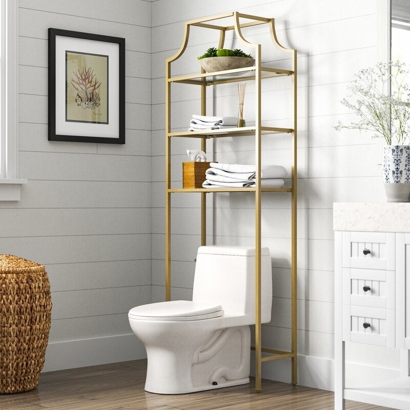 A very neat bathroom with a toilet and gold over-the-toilet storage