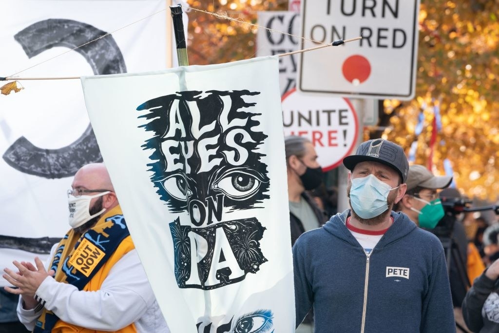 Man wearing a face mask holds sign that says, &quot;All Eyes on PA&quot;