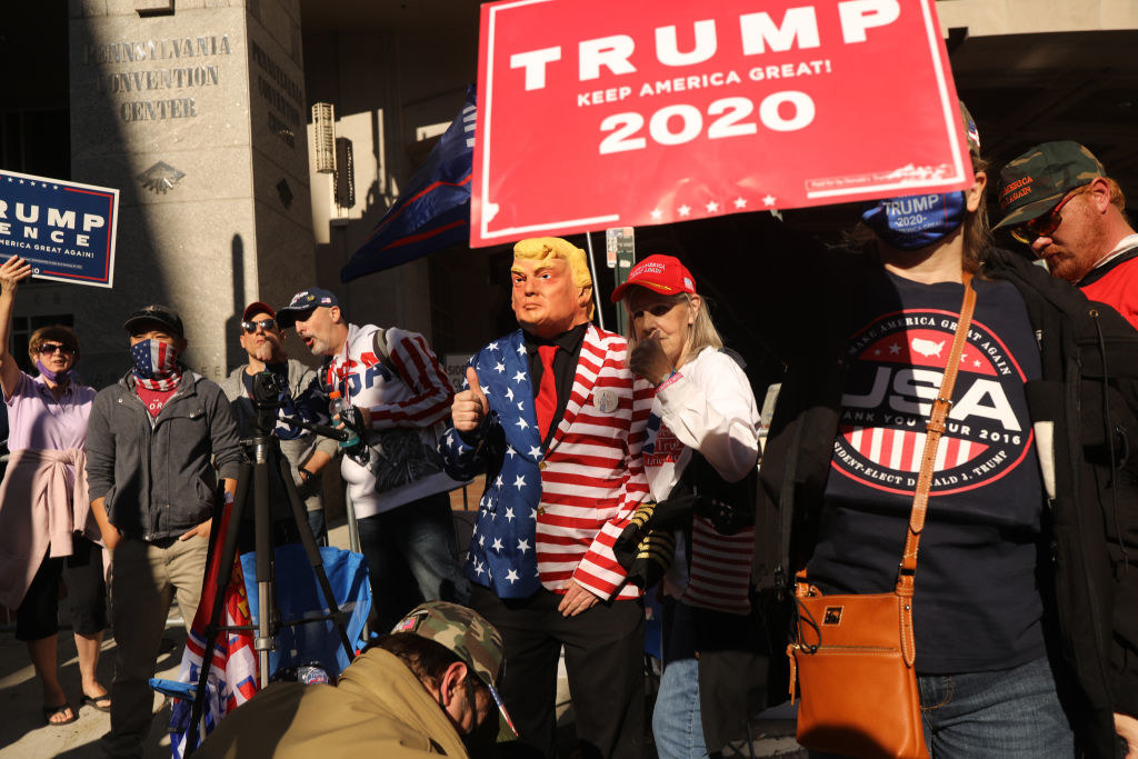 Man dressed in a suit with stars and stripes wearing a Trump mask posing next to several other pro-Trump protestors