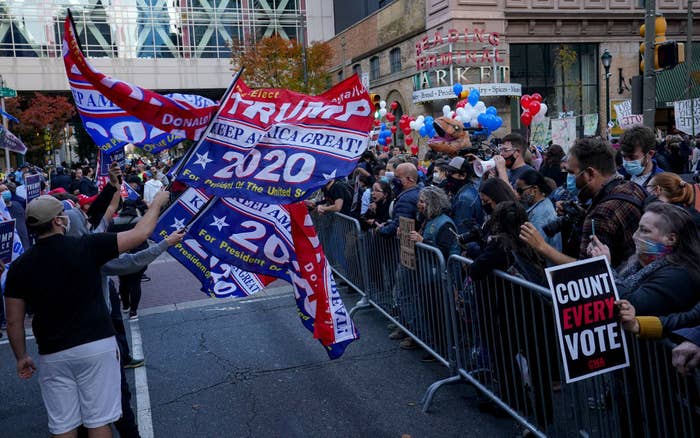 Pro-Trump protestors wave &#x27;Keep America Great!&#x27; flags while protestors in favor of continuing to count votes and photographers look on from the other side of a barricade