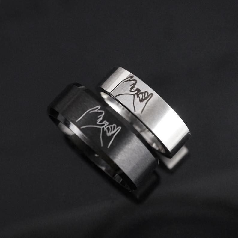 a black and metal ring with two hands pinky promising engraved on it