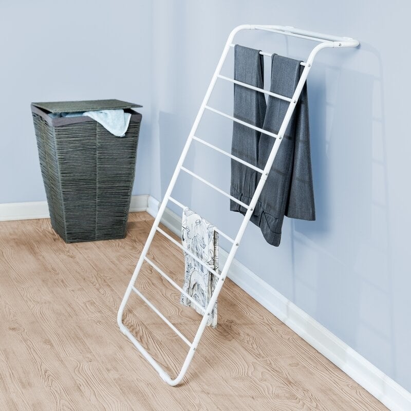 A white wire clothes dryer leaning on a blue wall with a hamper nearby