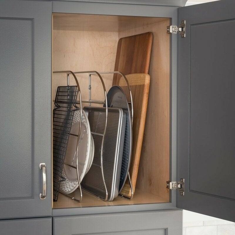 A kitchen cabinet with baking pans and cutting boards inside separated by metal wire dividers