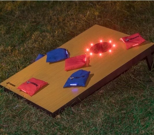 The cornhole board, illuminated, with bean bags on top