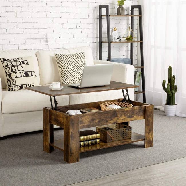 the dark wood coffee table with the top lifted and a laptop and mug on it