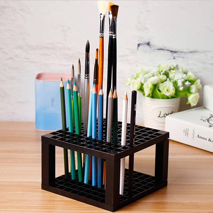 An art supply holder with several paintbrushes and pencil crayons inside