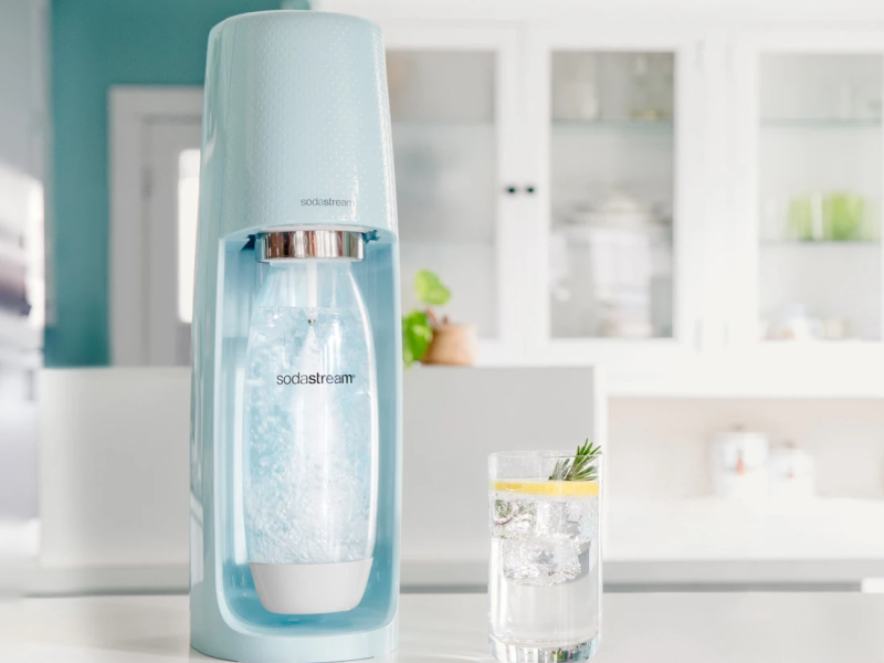 Mint blue SodaStream sitting out on a white counter next to a glass of carbonated water