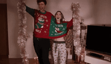 Zoe Sugg and Mark Ferris fall over while sharing a single tacky Christmas sweater and holding silver tinsel decorations.