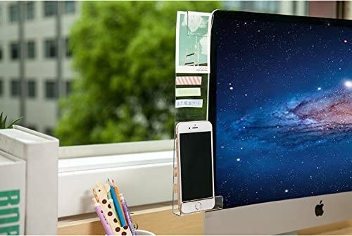 Close crop image of a desktop computer in front of a window; attached to the monitor is a clear memo board / phone holder