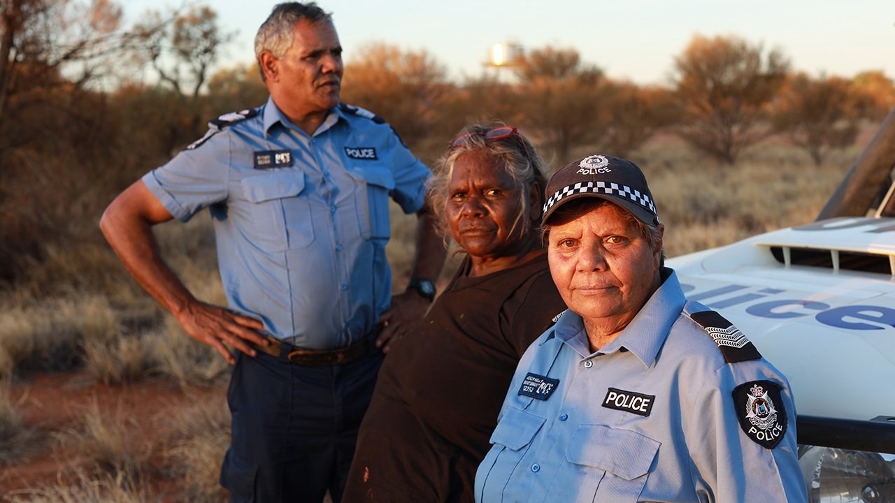 Two police officers and a woman standing in front of a police car in the Australian bush