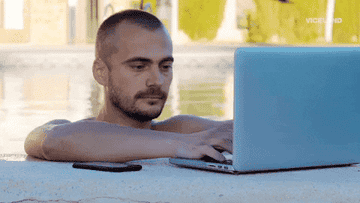 Man smiling and typing on a laptop by a pool