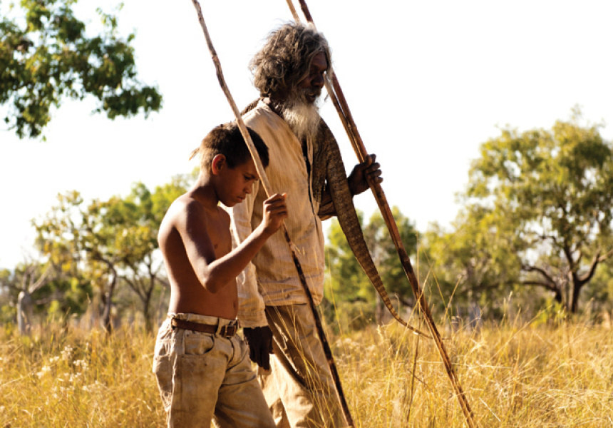 A young boy and his grandfather holding spears while walking in the Australian bush