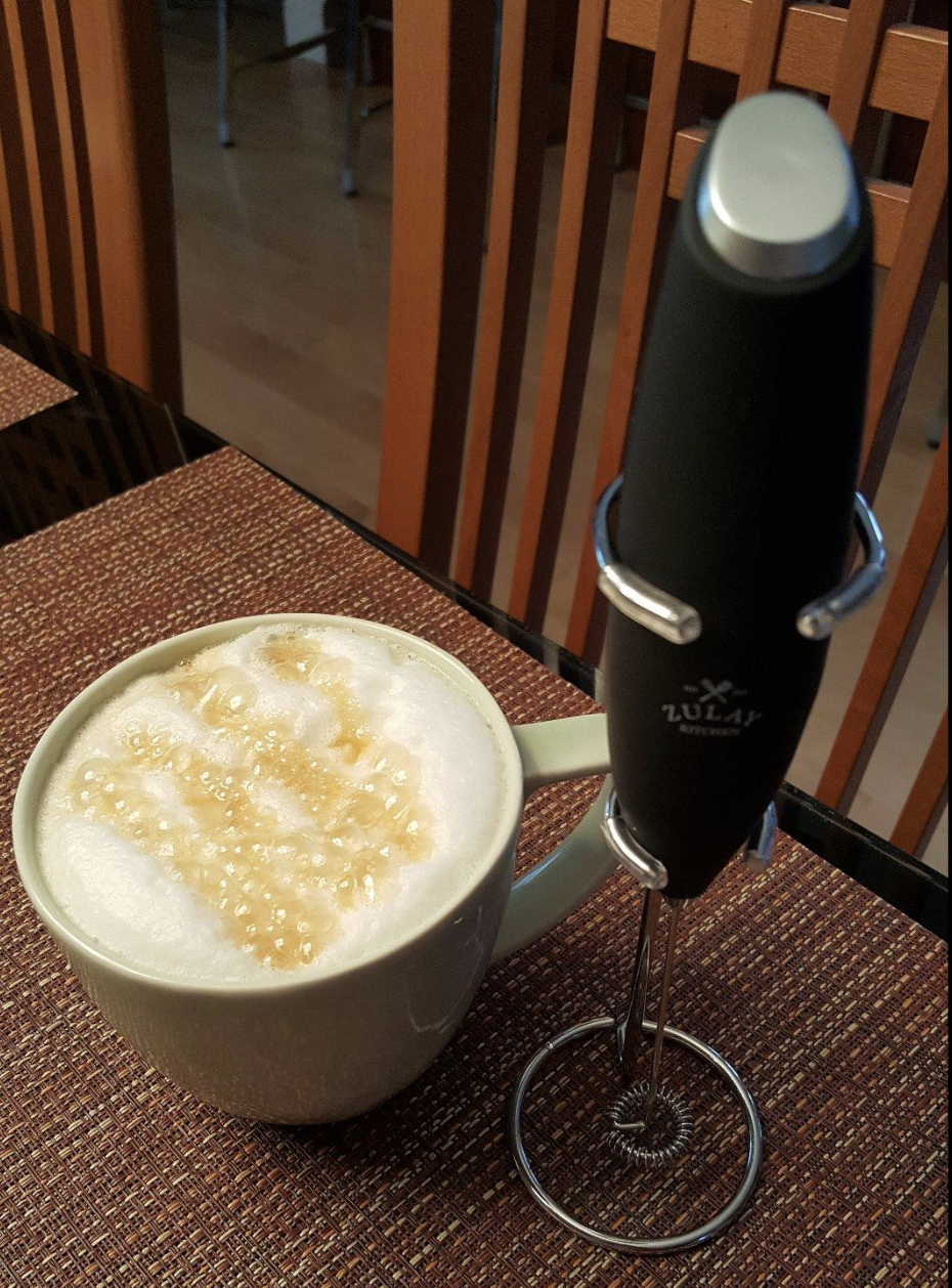 A black handheld frother propped next to a frothed cup of coffee 