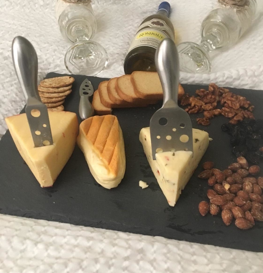 Reviewer pic of the black slate rectangle-shaped board  with a variety of cheese, crackers, and nuts on it with silver tools suck into the cheese
