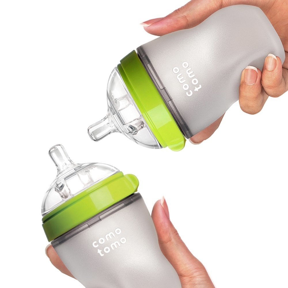 Model&#x27;s hands holding two baby bottles with lime green tops