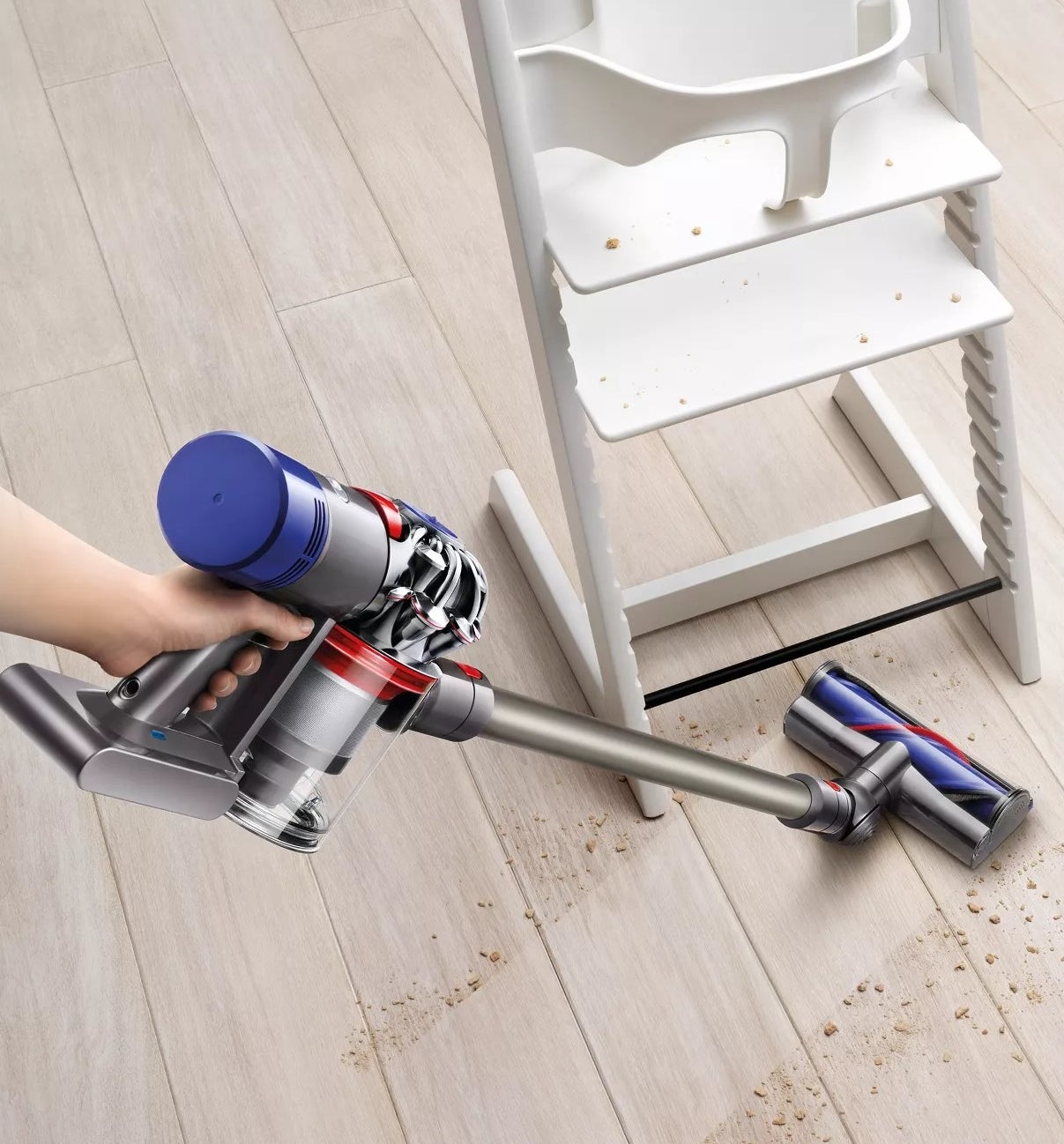 A model using the vacuum to clean the floor underneath a highchair 