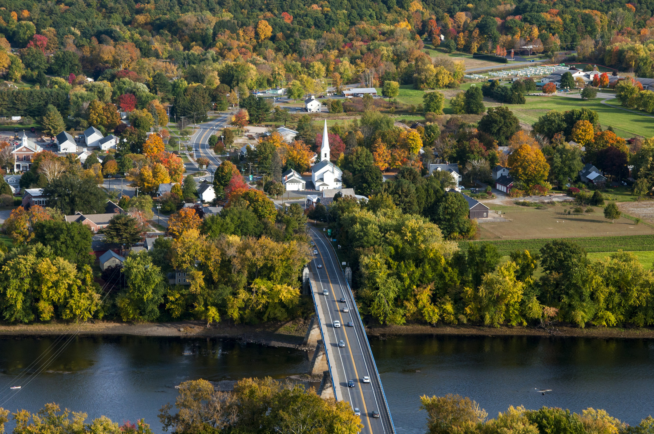 A drone shot of Mount Sugarloaf State Reservation with a bridge over the water and fall foliage beyond