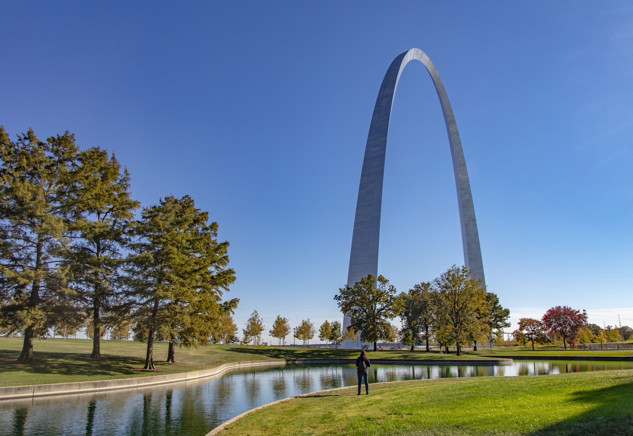 The gateway arch against a cloudless blue sky with grass and trees in the foreground