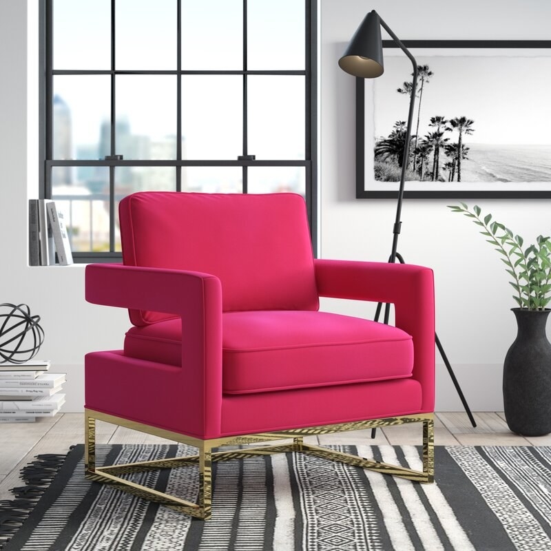 A bright pink accent chair with gold frame and legs