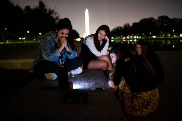 Leslie Luna, left, and friends sit near the Lincoln Memorial Reflecting Pool while watching President-elect Joe Biden and Vice President-elect Kamala Harris deliver remarks from Wilmington, Del.