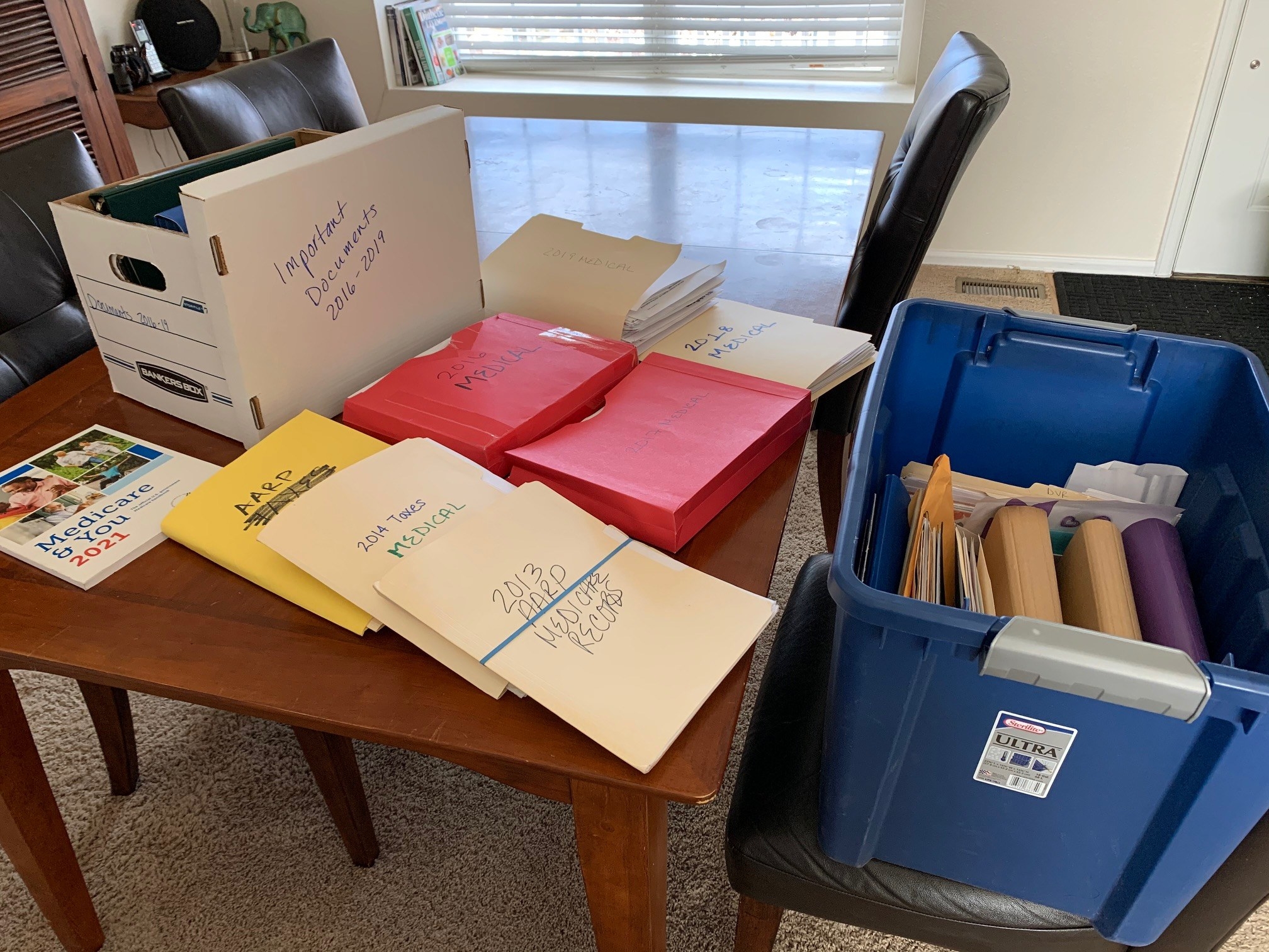 Piles of thick folders filled with medical records and labeled by year sit on a coffee table 