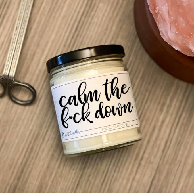 A candle on a counter with the label calm the f*ck down