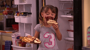 A girl messily eating a cake next to an open fridge